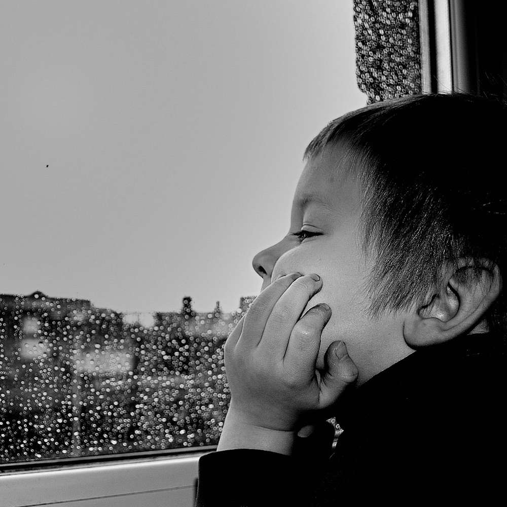 ein Kind schaut durch eine nasse Fensterscheibe nach draußen