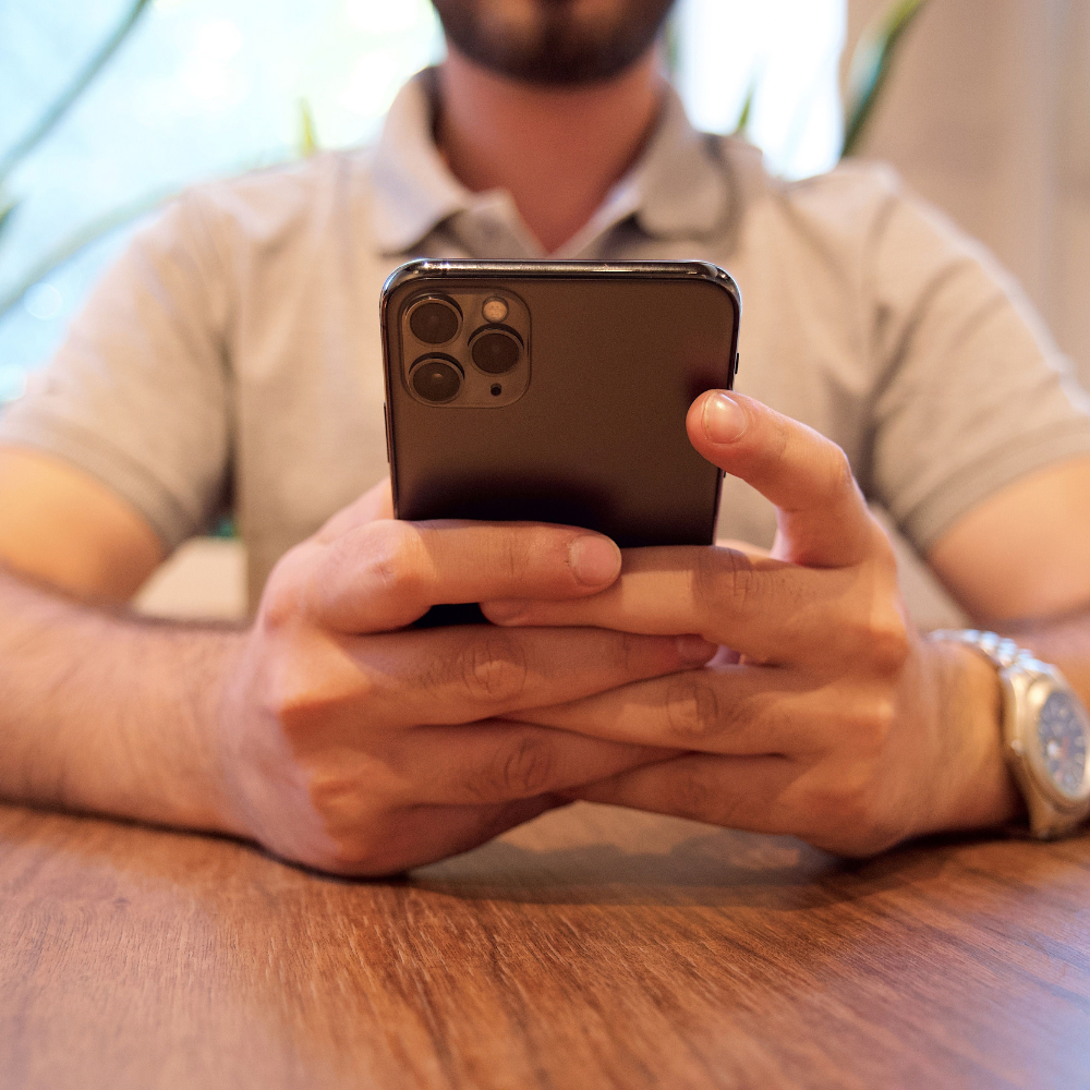 Ein Mann sitzt an Tisch und hält Smartphone mit beiden Händen
