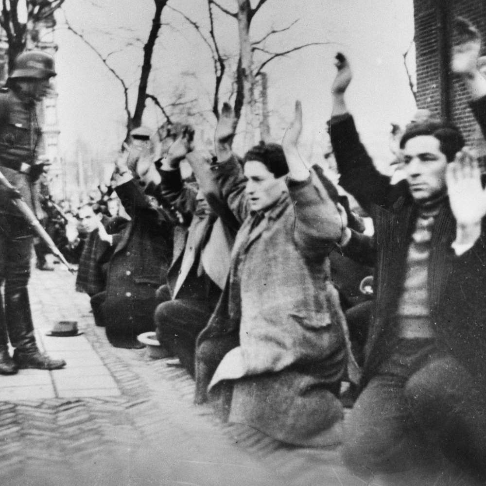 Personen knien vor bewaffneten Soldaten und halten die Hände hoch