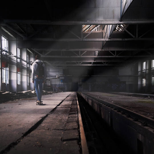 Skateboardfahrer in altem Bahnhof von hinten